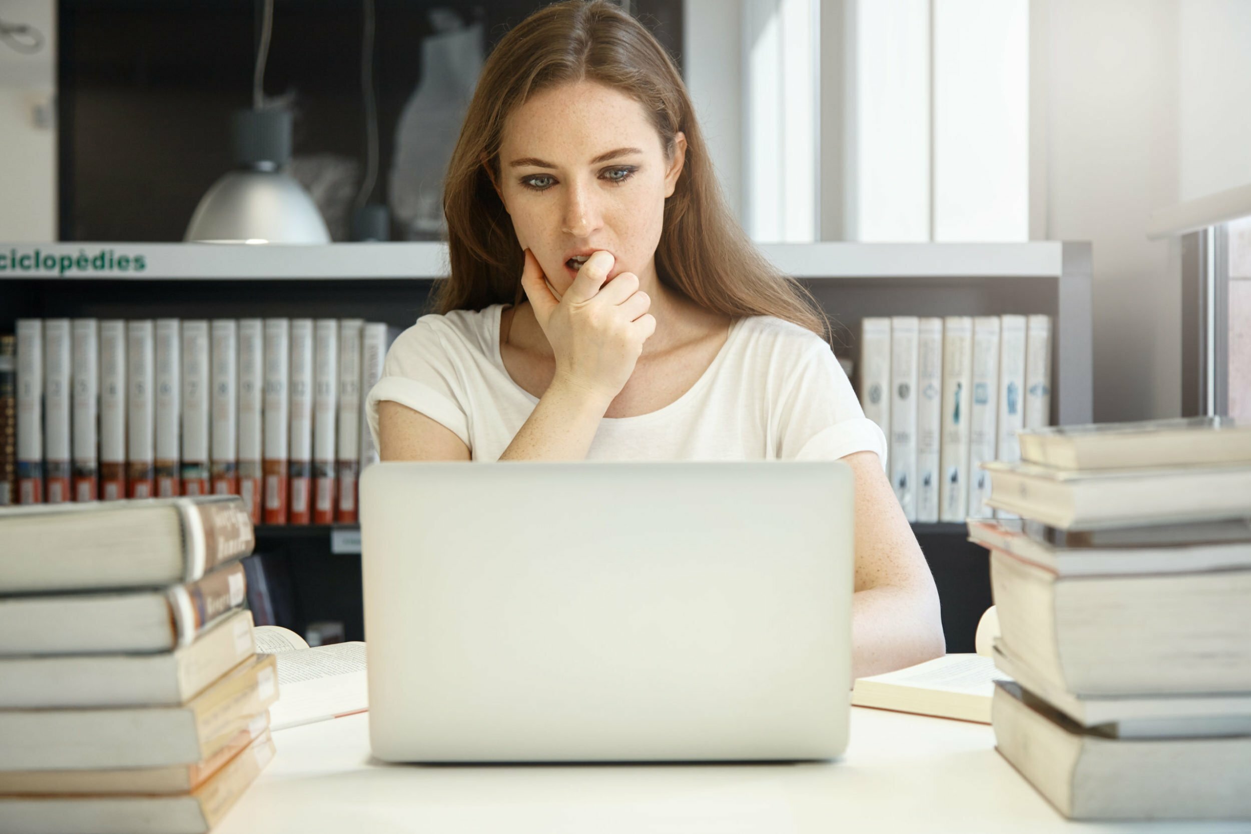 a woman sitting at a desk with a laptop and a stack of books